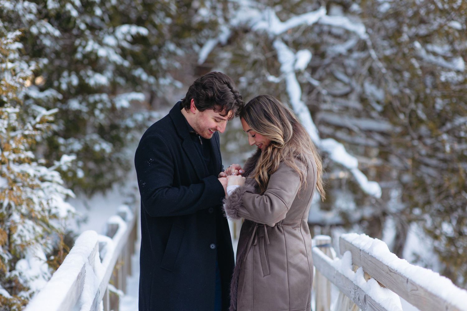 A romantic winter scene with a couple embracing on a snowy path surrounded by trees.