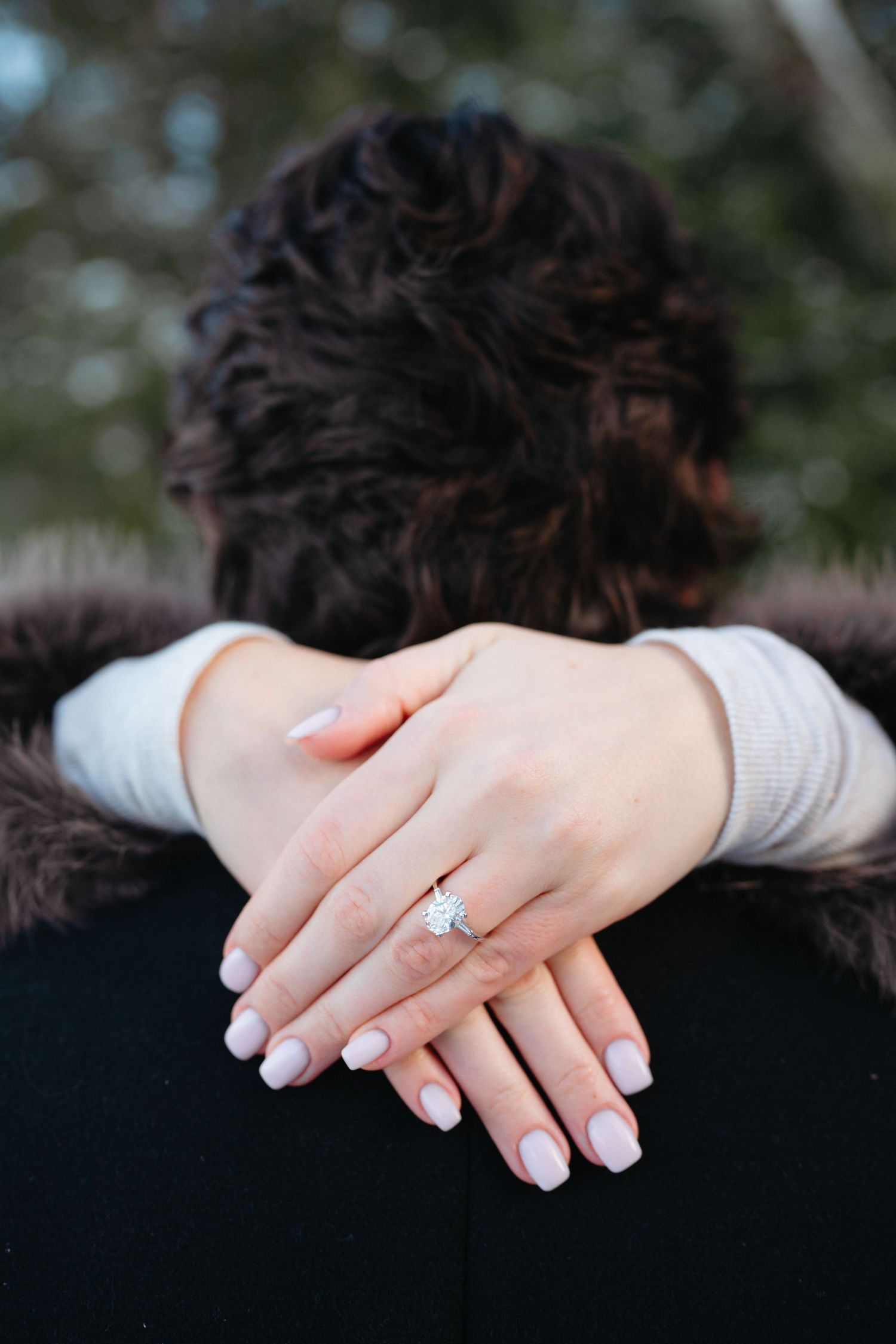 Close-up of freshly manicured hands with French tips and an engagement ring resting on a black coat.