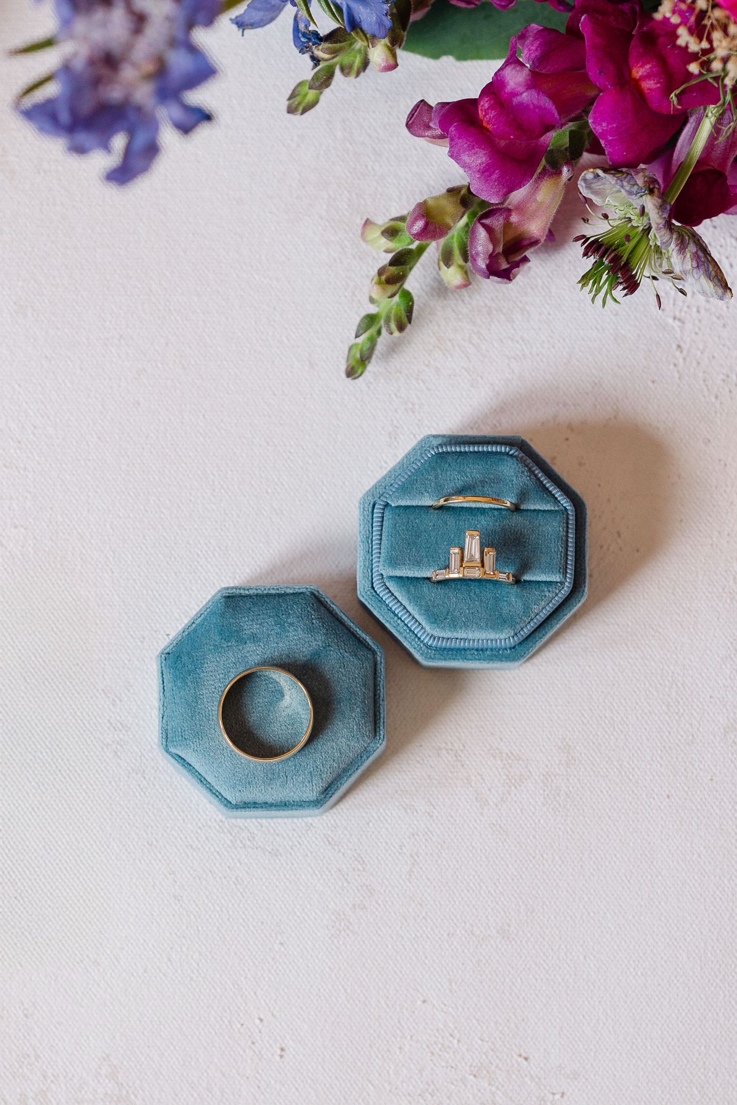 A sparkling diamond engagement ring sits in a turquoise velvet hexagonal ring box on a light surface.