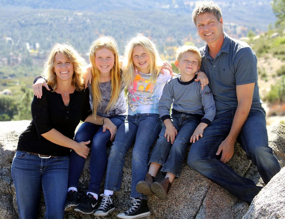Family group sitting together on rocky outcrop with mountain vista in background.