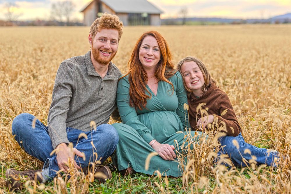 Family lying together in golden wheat field during sunset photoshoot.