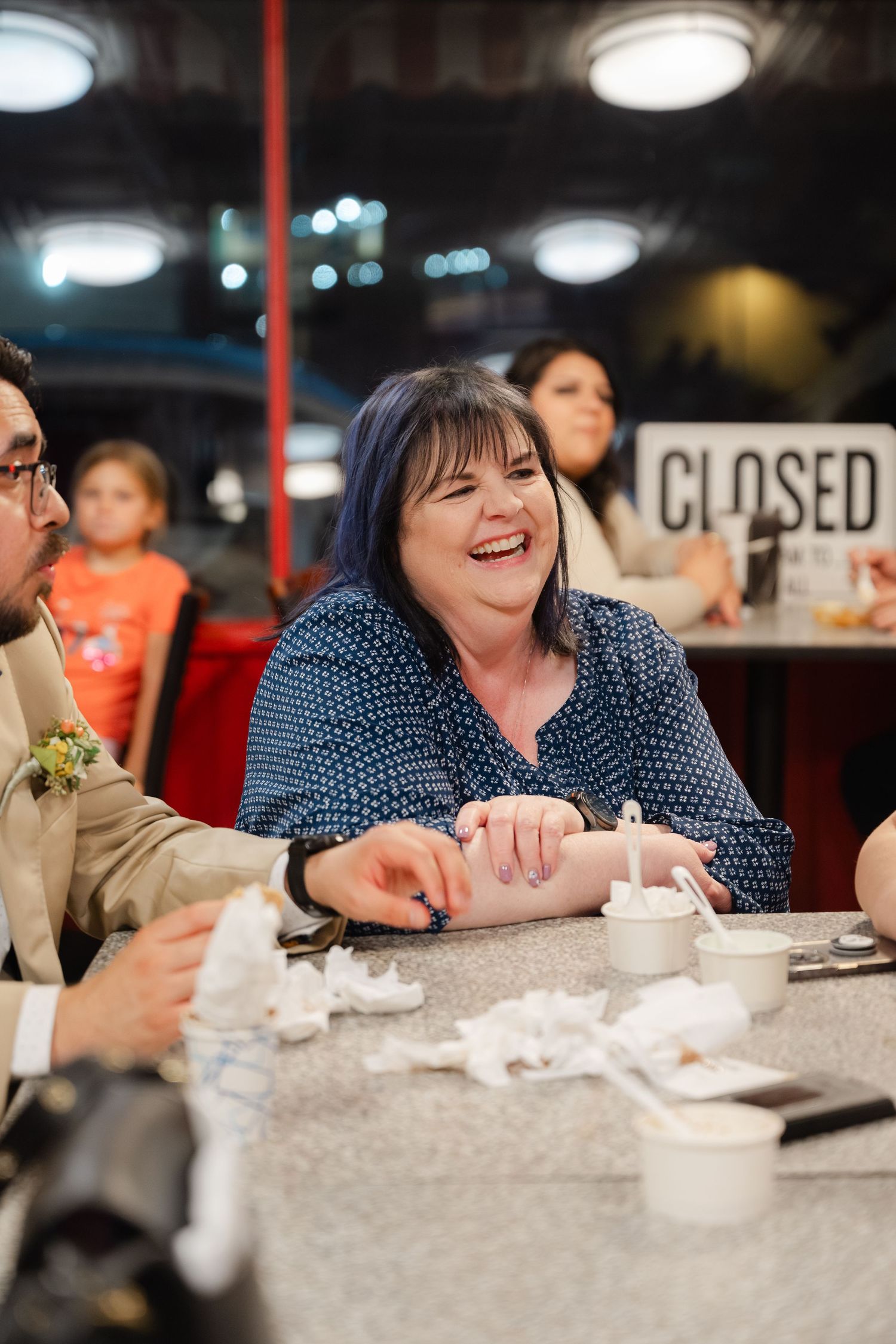 People enjoying a meal together at a restaurant table with a polka dot pattern dress visible in the frame.