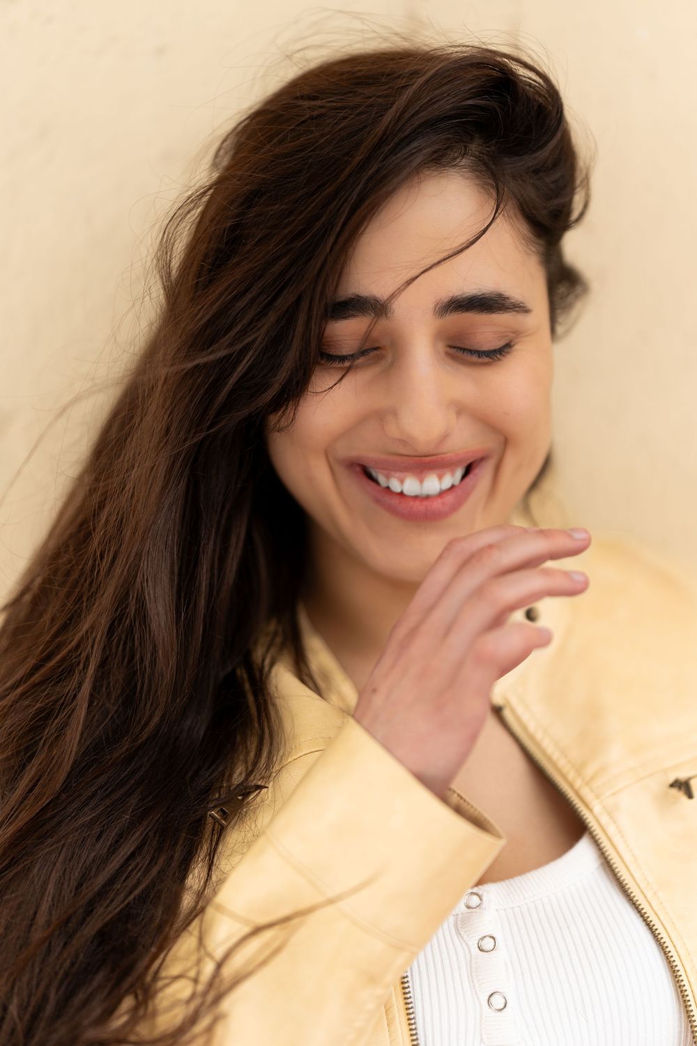 A sequence of candid photos showing someone with long dark hair laughing and covering their smile in a white top.
