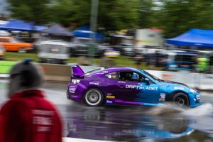 Blue and purple race car drifting on wet track during motorsport competition.