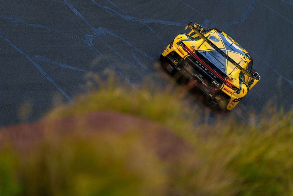 A yellow Porsche 911 GT3 races along a winding mountain road with dramatic storm clouds in the background.