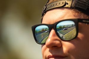 A closeup view of sunglasses reflecting a road and blue sky on a sunny day.