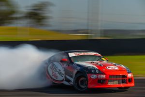 Red sports car drifting with smoke trails on race track.