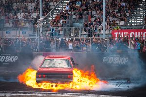 Red muscle car performs a burnout on dragstrip with smoke and flames coming from the exhaust.