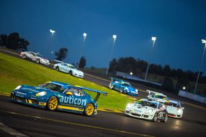 Race cars competing on an illuminated track at night with vibrant blue and yellow race cars in the foreground.