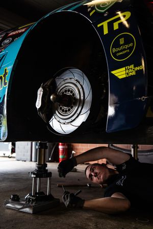 Mechanic examining car brake rotor and suspension system during maintenance work in auto repair shop.