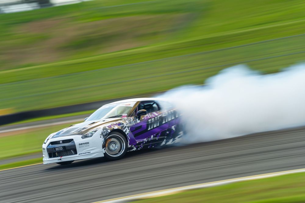 Drag racing car drifting on track with smoke trailing behind as it performs a high-speed turn.