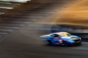 Motion-blurred race car speeds around track with colorful livery creating dramatic light trails at dusk.