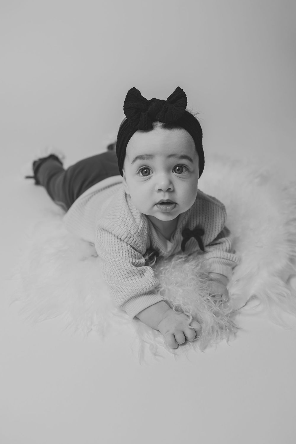 Black and white portrait series of a baby lying on soft white fur wearing a gray sweater.