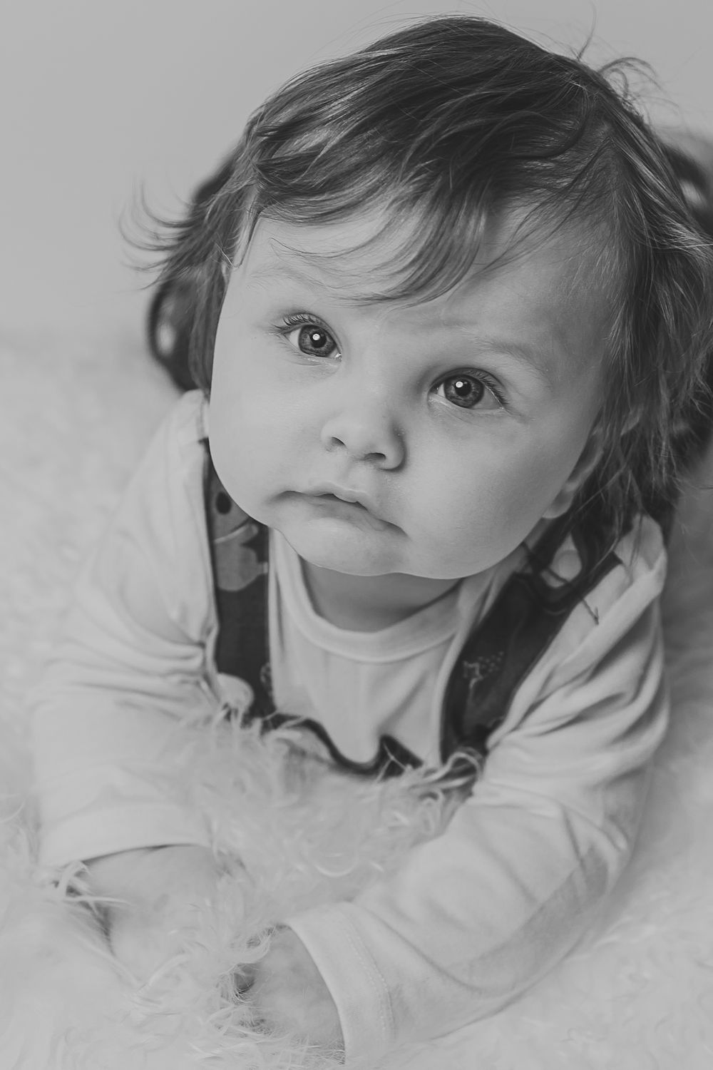 Black and white portrait of a baby in white clothing lying on a soft textured surface.