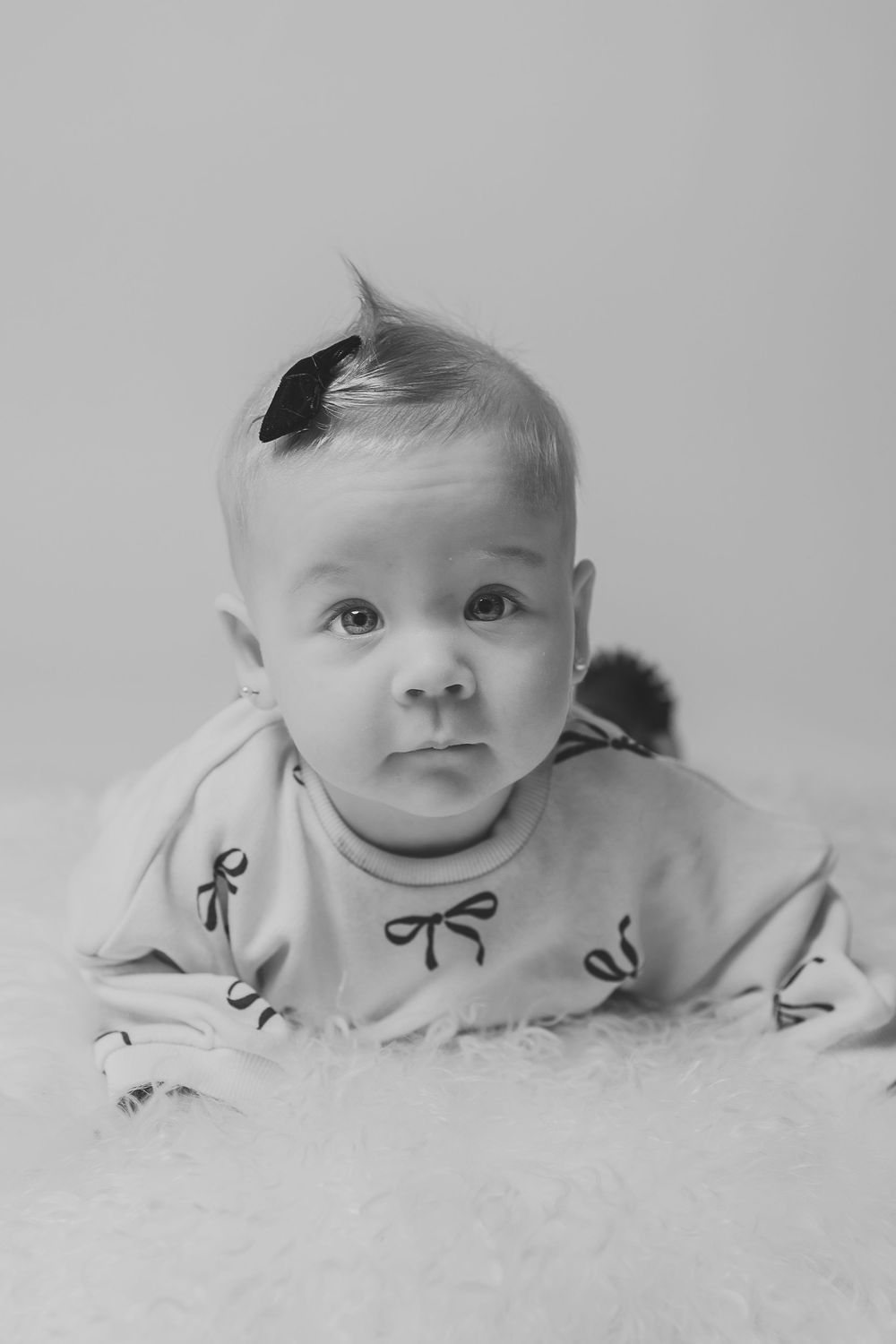 A series of black and white photos showing a baby lying on white bedding with a sweet smile and bow pattern clothing.