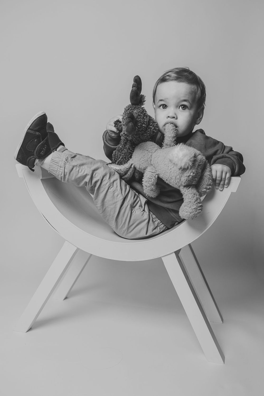 A series of black and white photos showing a baby lying on a curved white surface with a stuffed animal.