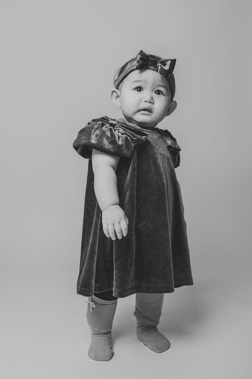 Black and white photo series showing a small child in a velvet dress sitting and posing in different positions.