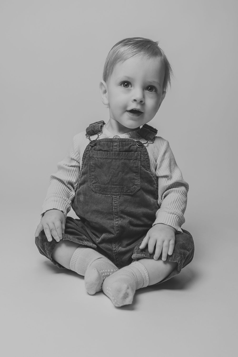 A series of black and white photos showing a baby in corduroy overalls sitting and posing in different positions.