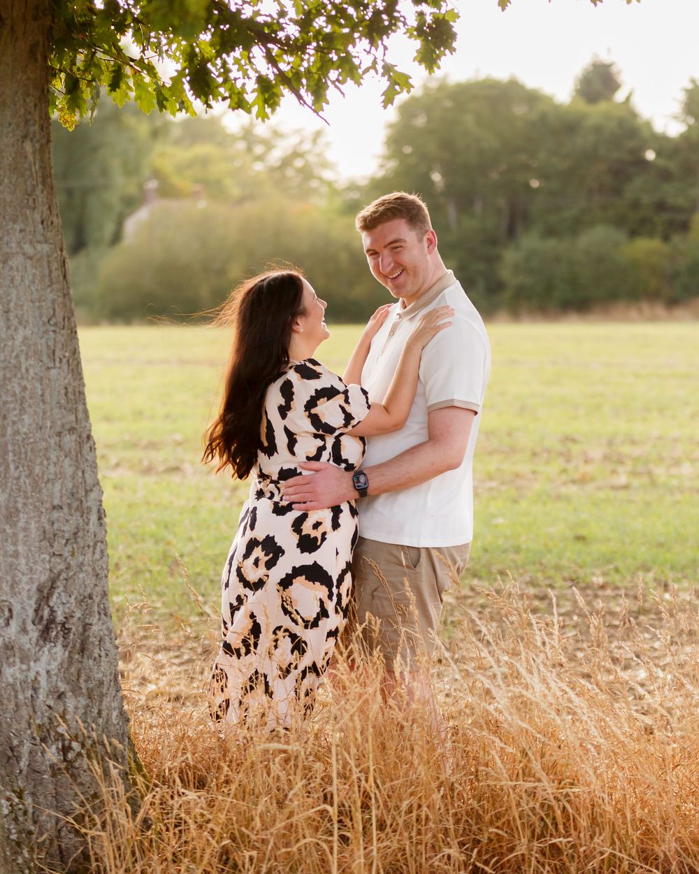 A couple shares joyful moments together while standing in a sunlit field of tall golden grass.