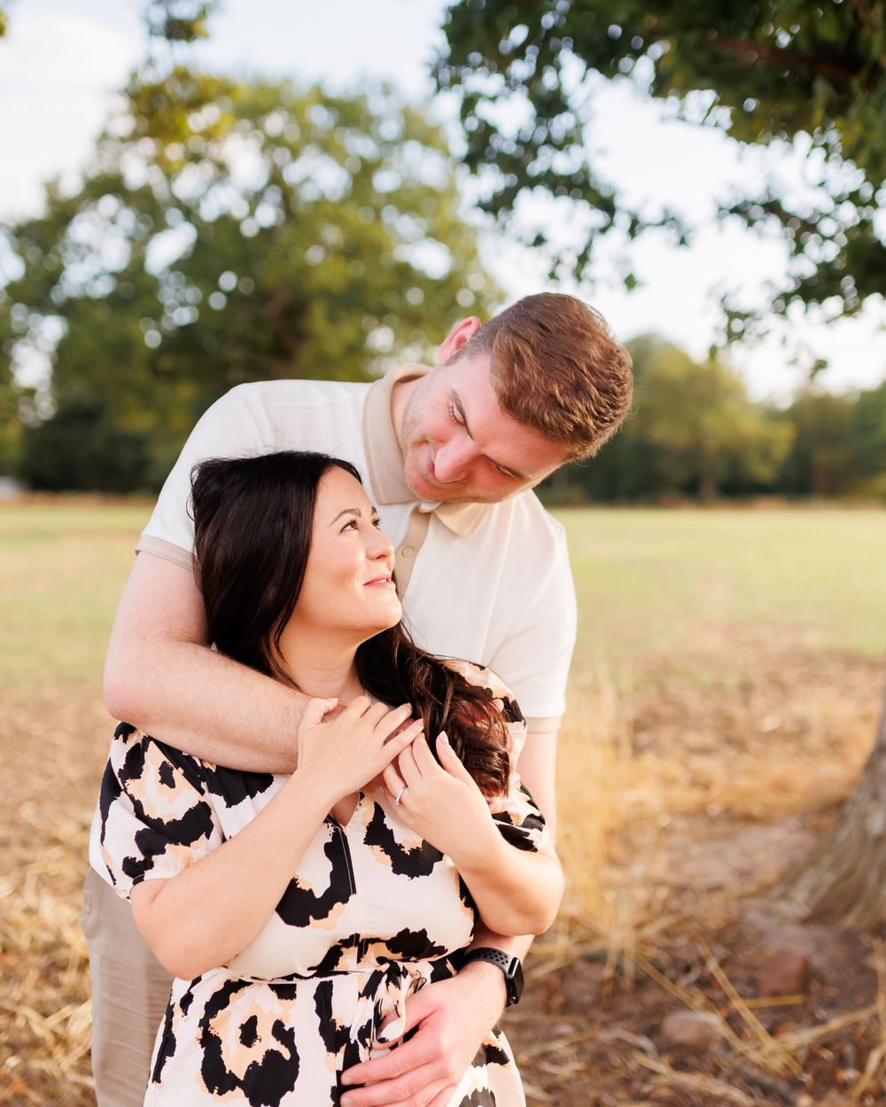 A romantic couple embraces in a sunlit field during a golden hour photo session.