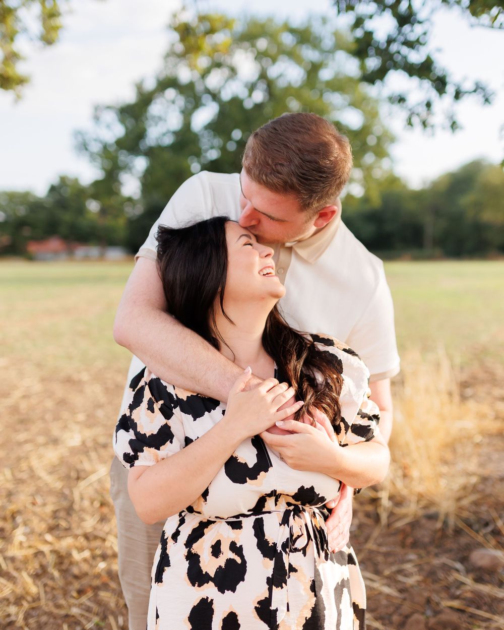Tender embrace photographed in warm sunlight with rustic field and foliage backdrop.