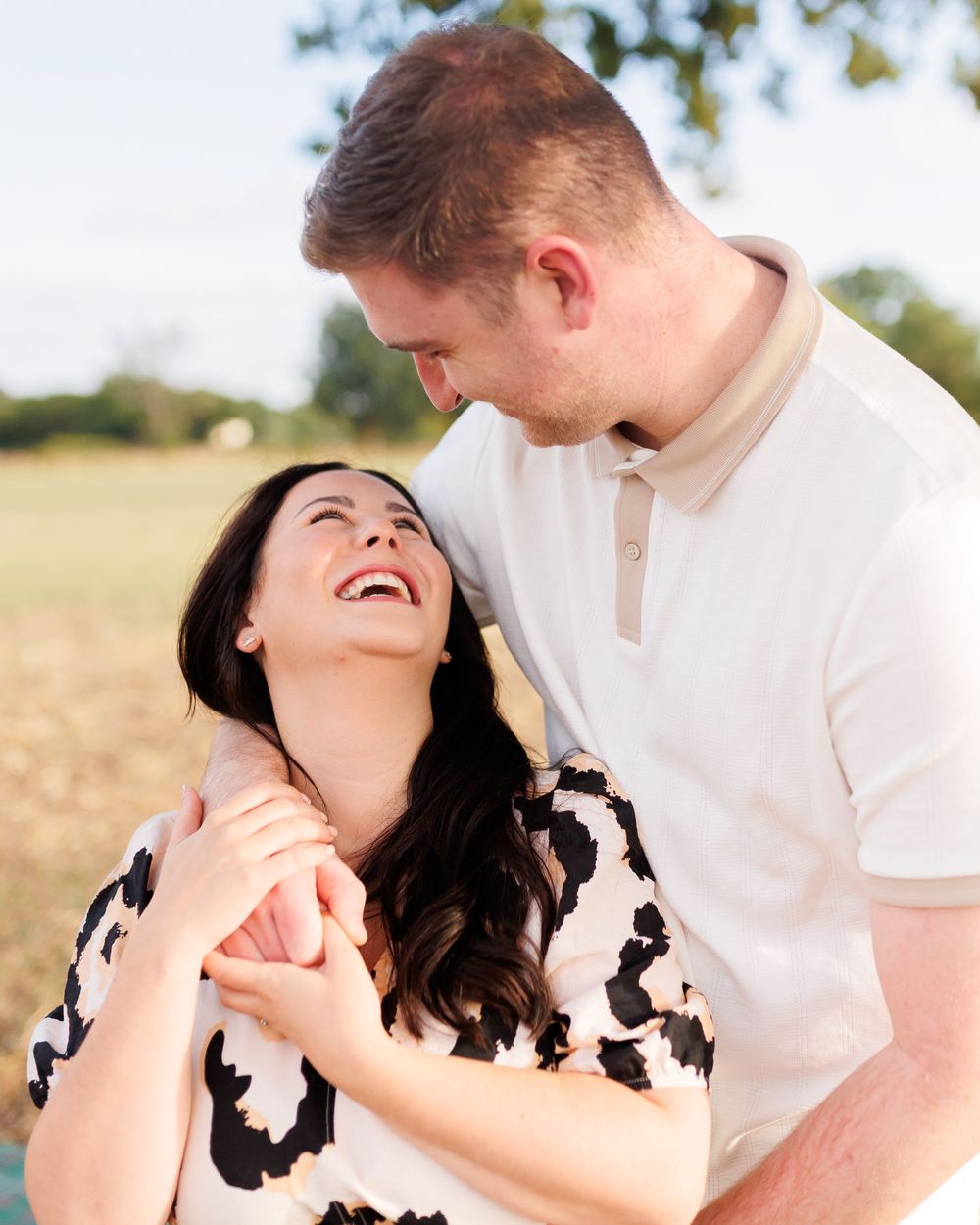 A couple laughs together in a series of candid romantic outdoor photos in golden sunlight.