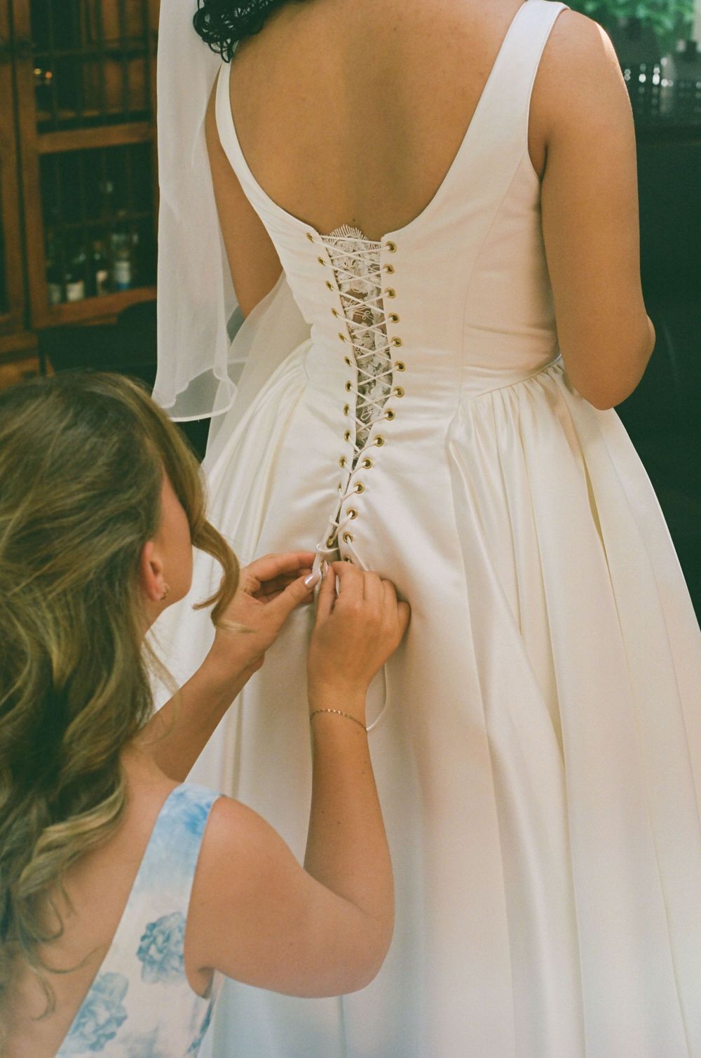 Detail shot of corset-style back lacing on white wedding dress being adjusted.