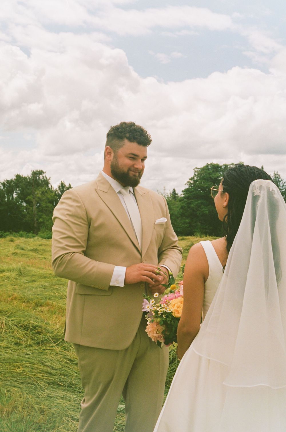Newlyweds share an intimate moment in a sunny field with tan suit and white wedding dress.
