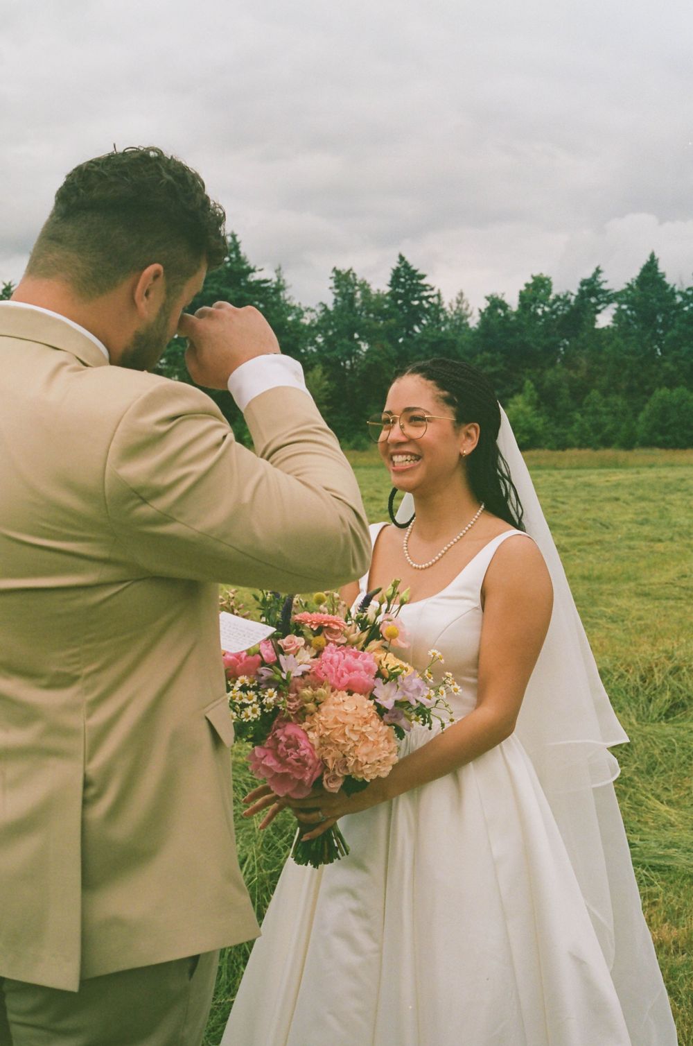 Close-up of wedding couple with pink bouquet sharing emotional moment outdoors.