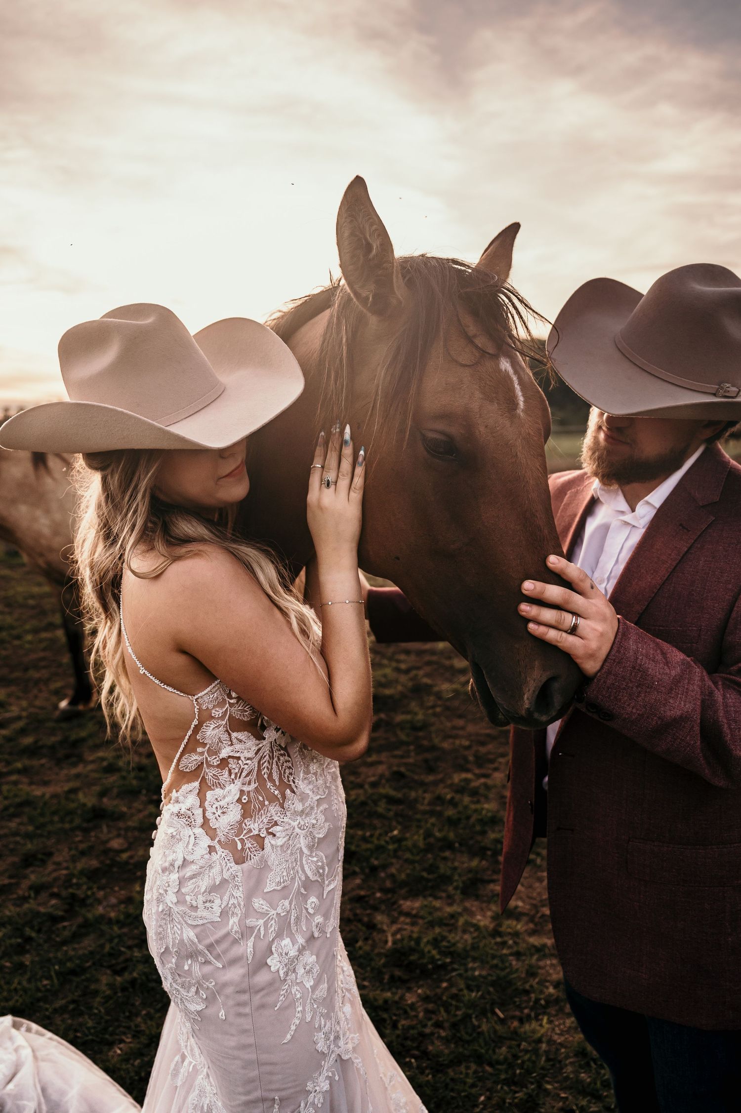A romantic outdoor photoshoot featuring a white lace dress and cowboy hat against a moody sunset sky.