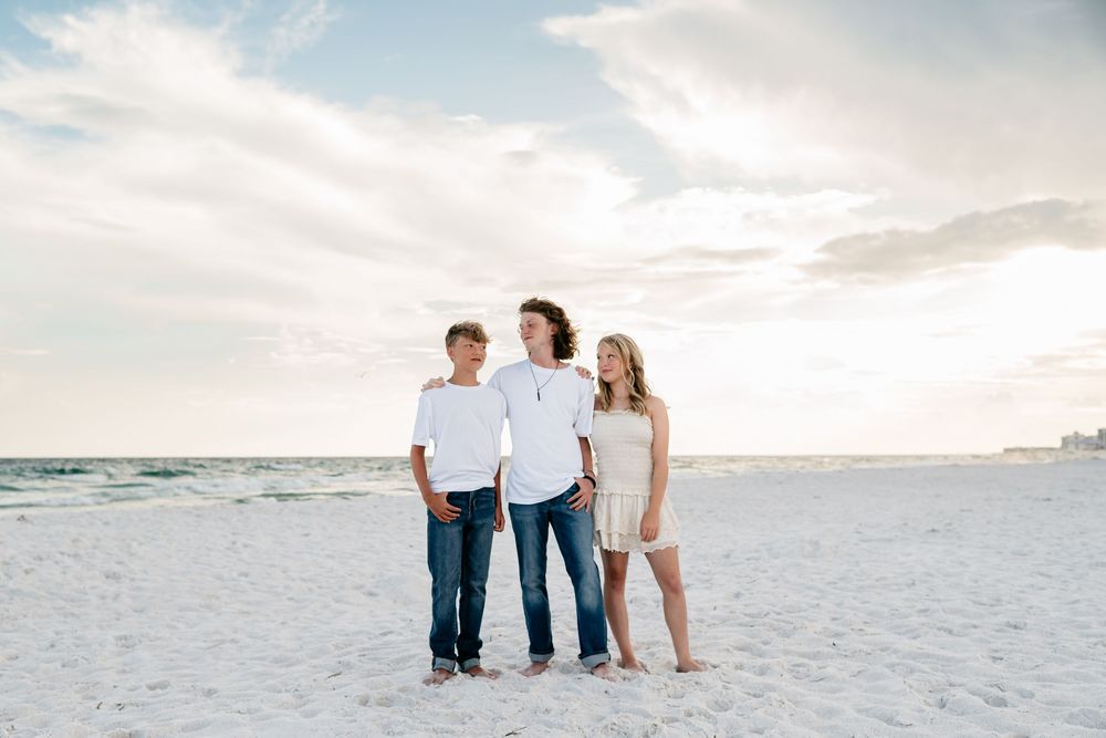A group of people walk together on a pristine white sandy beach at sunset.