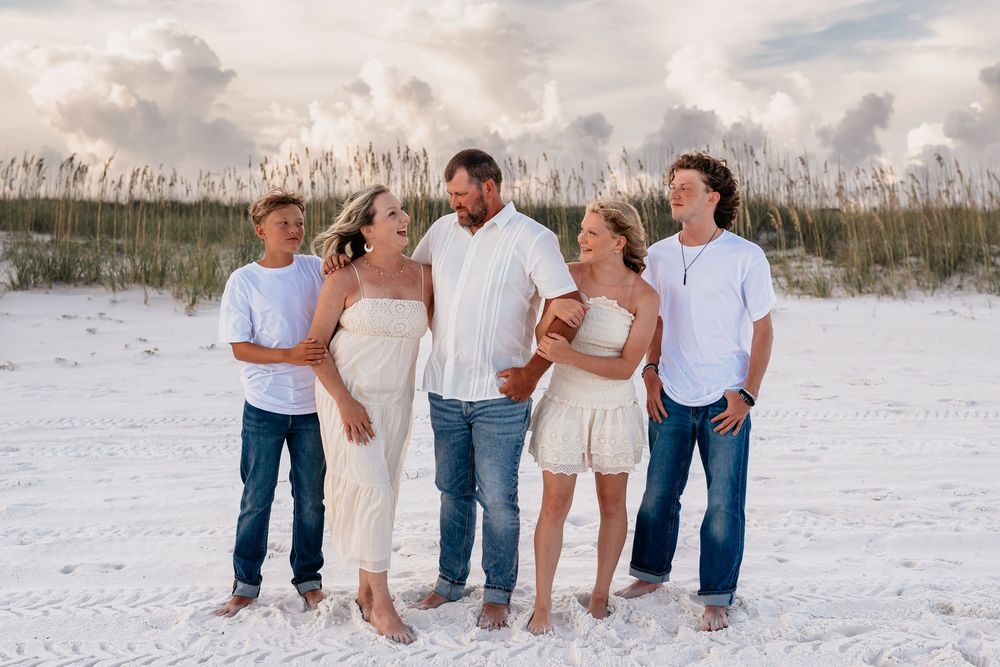 A series of photos showing a family wearing blue denim and white outfits posing together on a sandy beach.