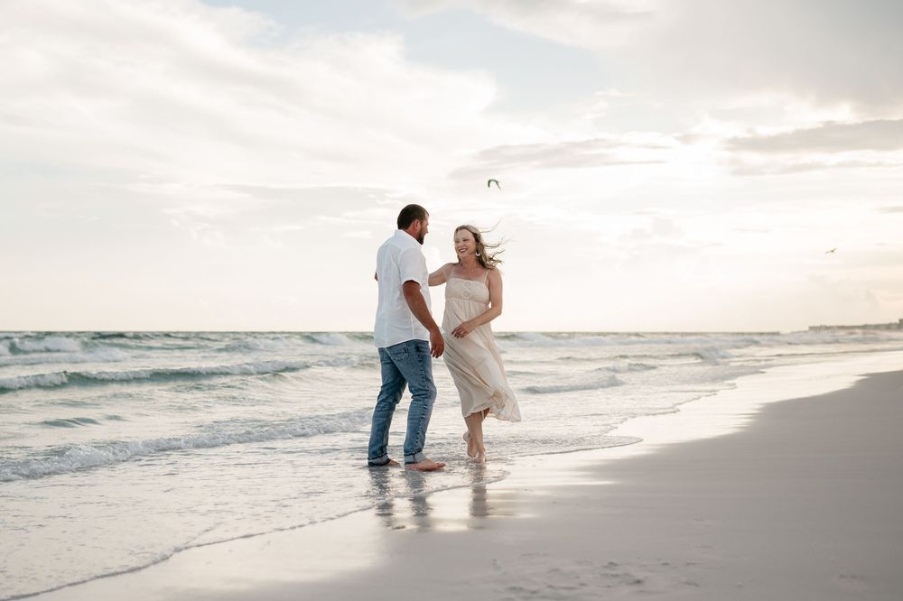 Two people sharing a romantic moment on a sandy beach at sunset with waves rolling in the background.