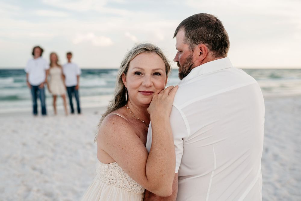 A romantic couple shares an intimate moment together on a sunny beach with waves crashing behind them.
