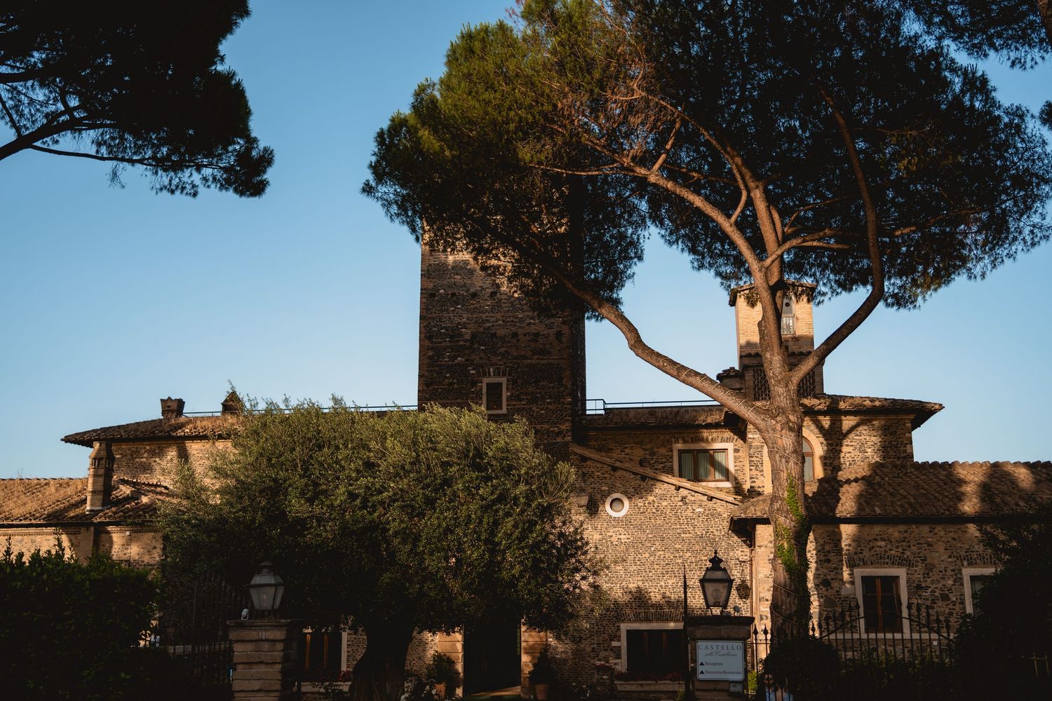 Historic Italian villa with stone architecture and cypress trees against blue sky.