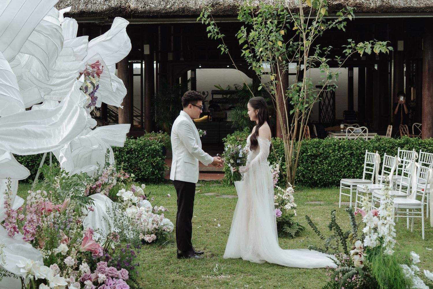 Bride and groom holding hands at outdoor garden wedding ceremony with white floral backdrop.