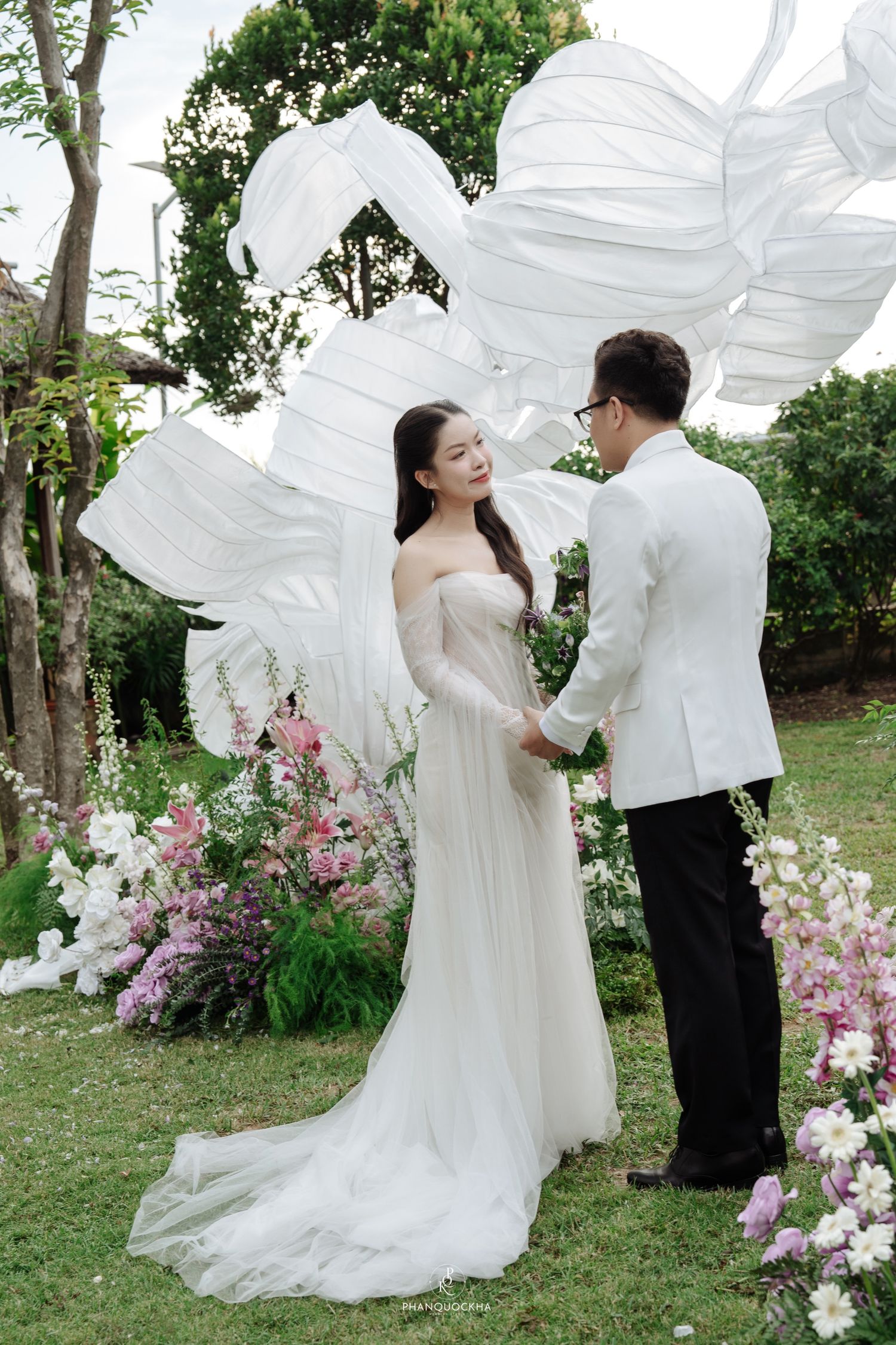 Bride and groom holding hands at outdoor wedding altar surrounded by pink and white flowers.