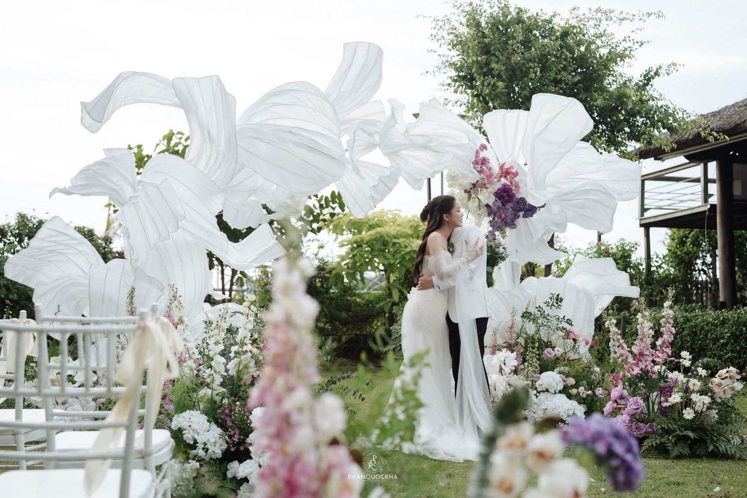 Bride and groom sharing kiss at outdoor garden wedding with white floral installations.