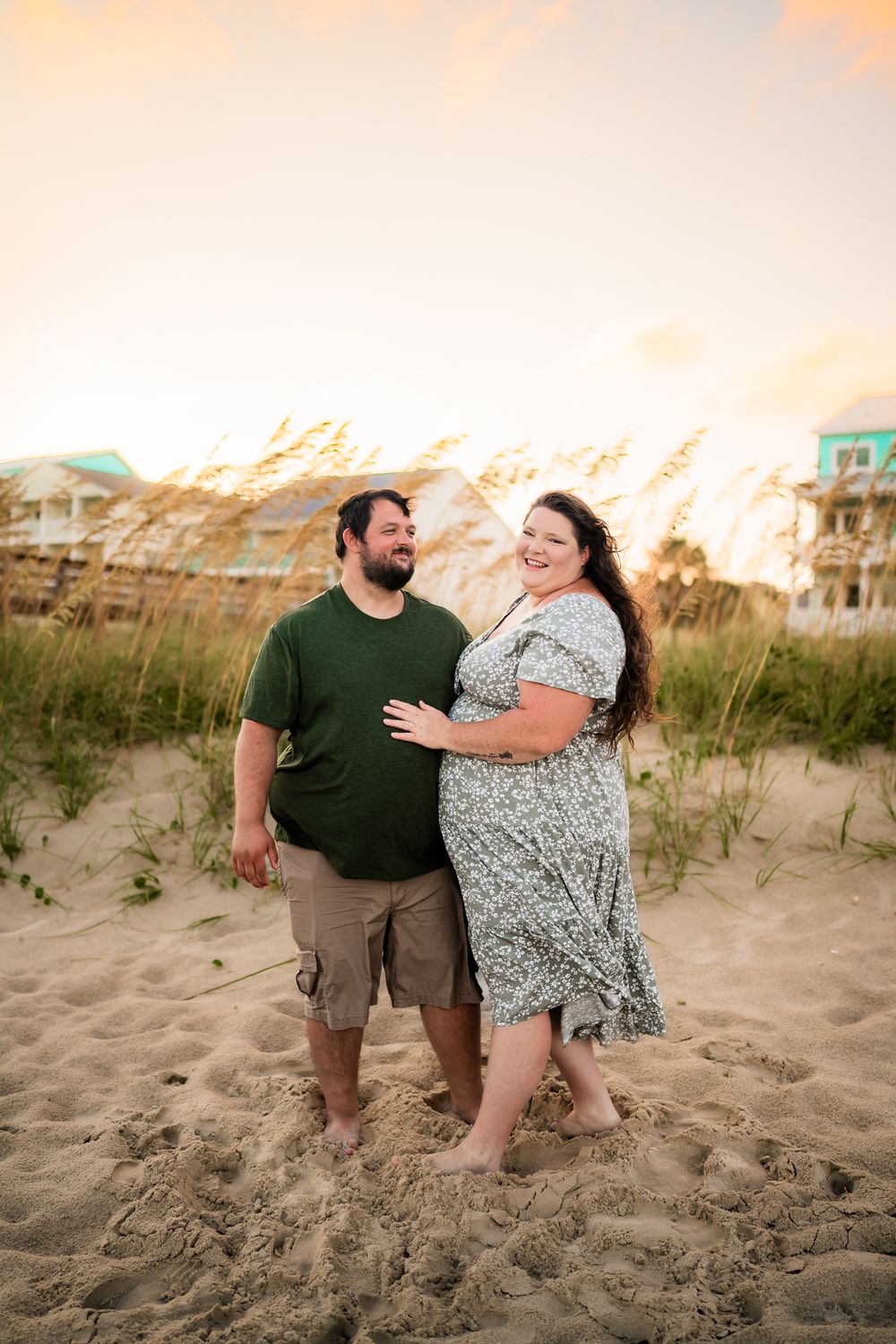A couple shares a playful moment together on sandy beach dunes during golden hour sunset.