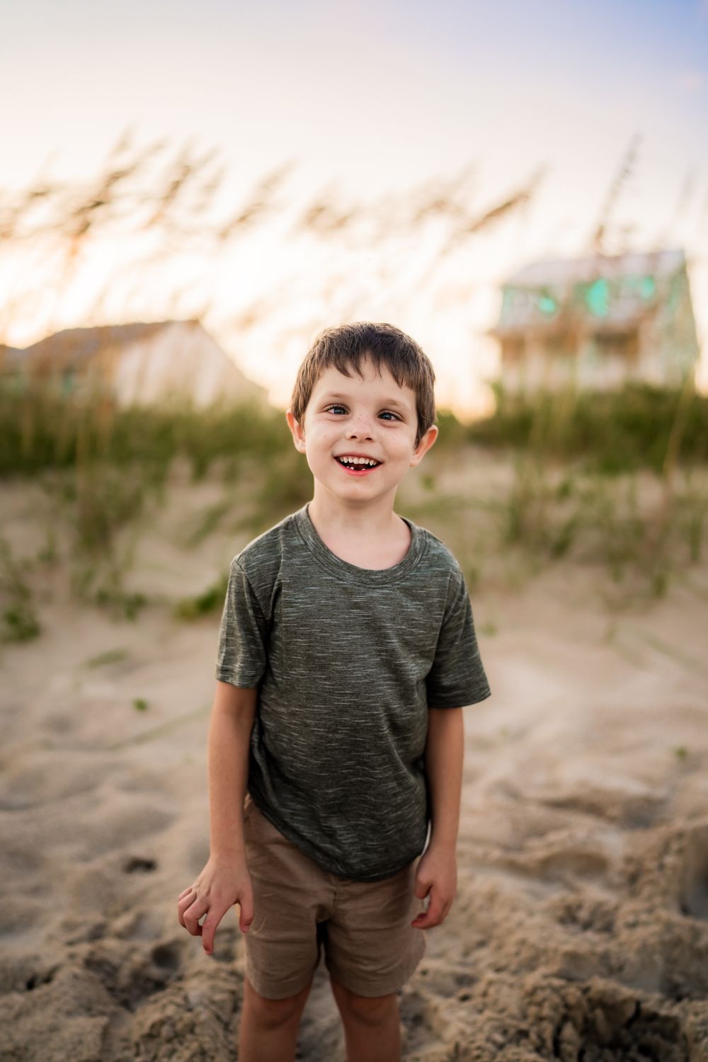 A young child smiles brightly while playing on beach sand dunes at dusk.