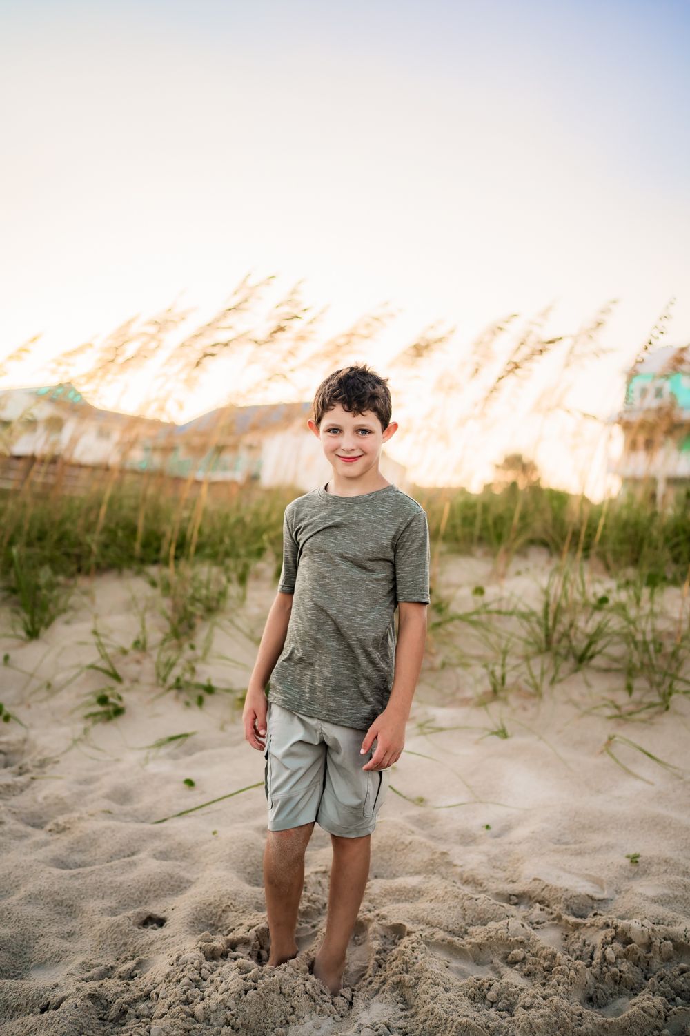 A young child enjoys playing in coastal sand dunes with beach grass and soft sunlight during golden hour.