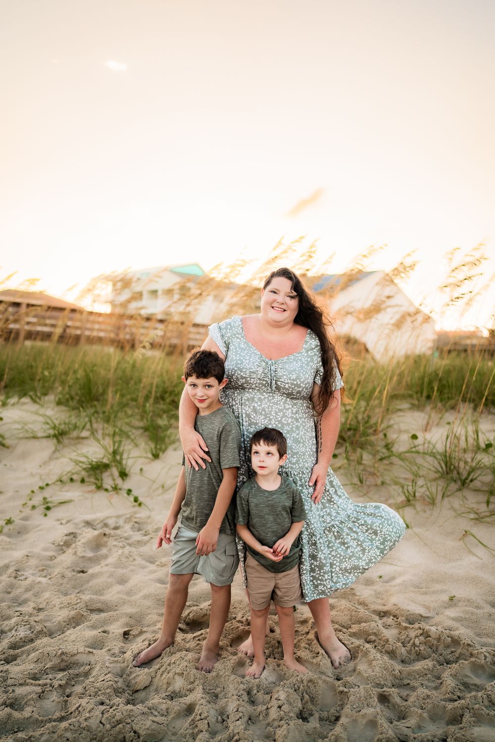 Family poses on sandy beach dunes at sunset in coordinated green and blue outfits.