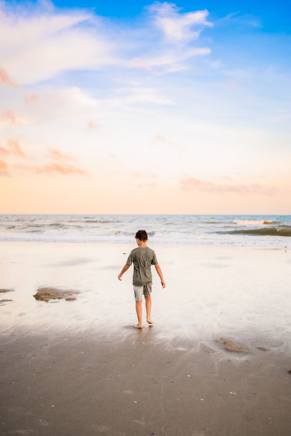 A series of photos showing someone walking through shallow ocean waves at sunset on a sandy beach.