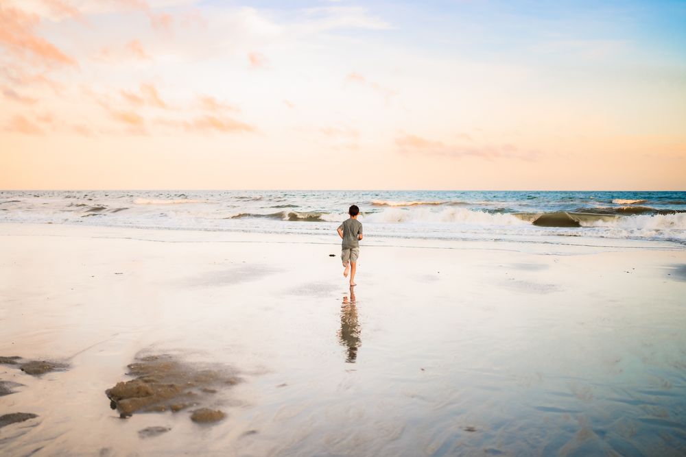 An expansive beach shoreline at sunset with gentle waves and footprints in the wet sand.