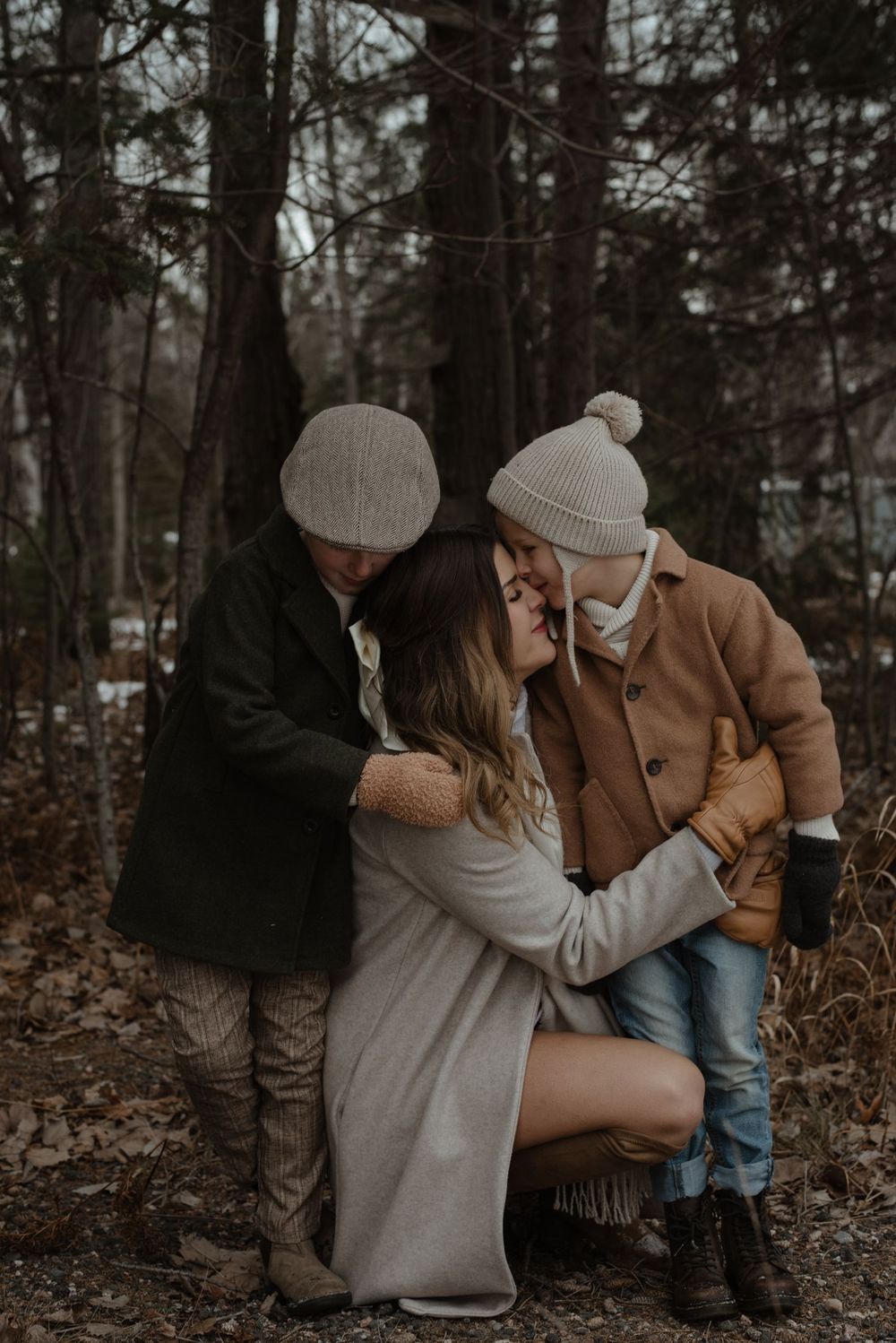 Intimate autumn forest scene featuring a family embrace in warm winter clothing and beanies.