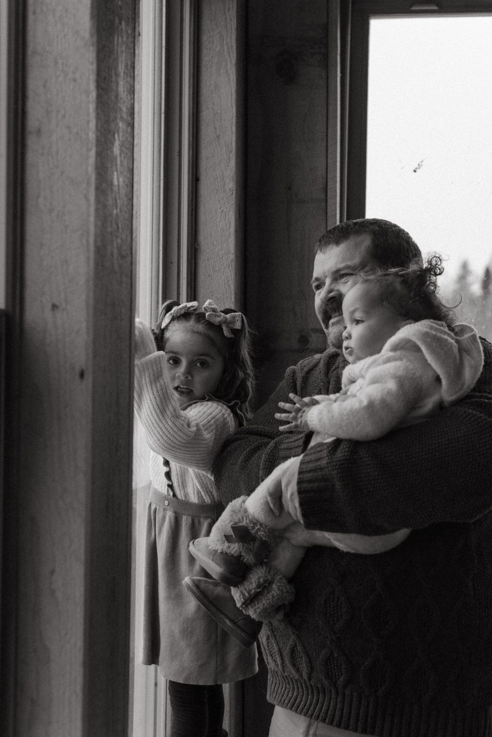 A black and white image of a family looking out a window together on a winter day.