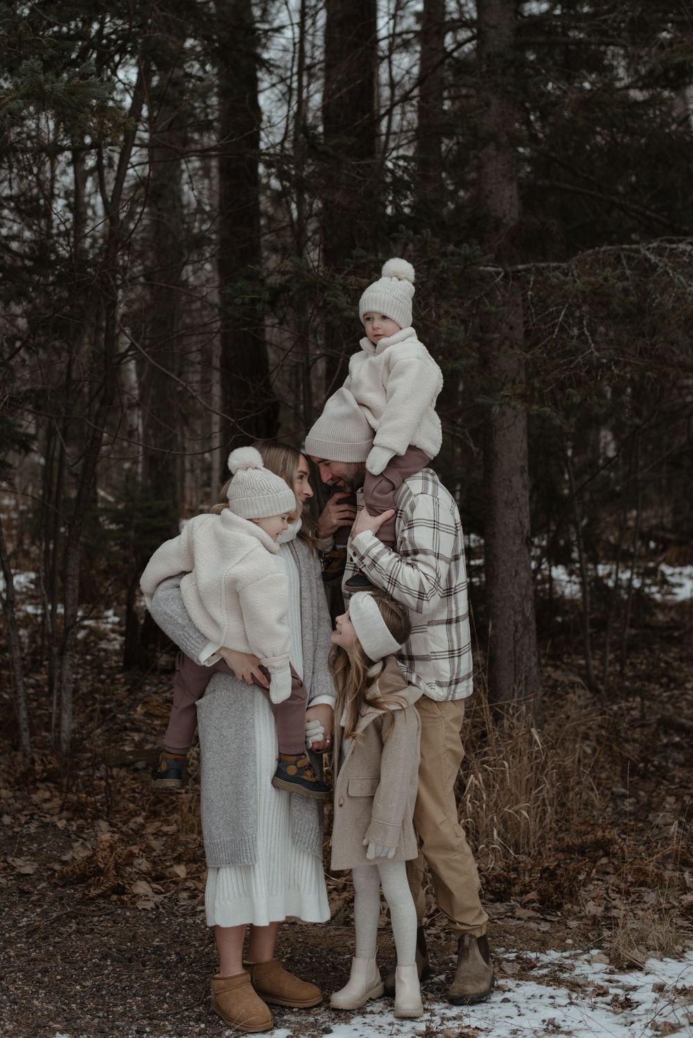 A family in matching white winter outfits poses together in a snowy forest setting.