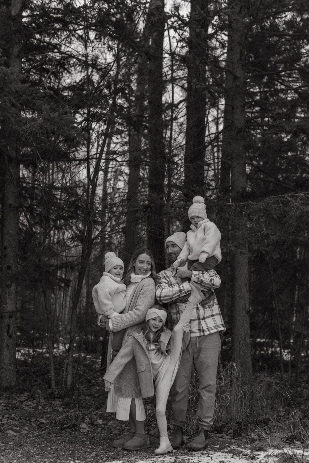 A black and white photo of a family of five standing together in a winter forest wearing warm coats and winter clothing.