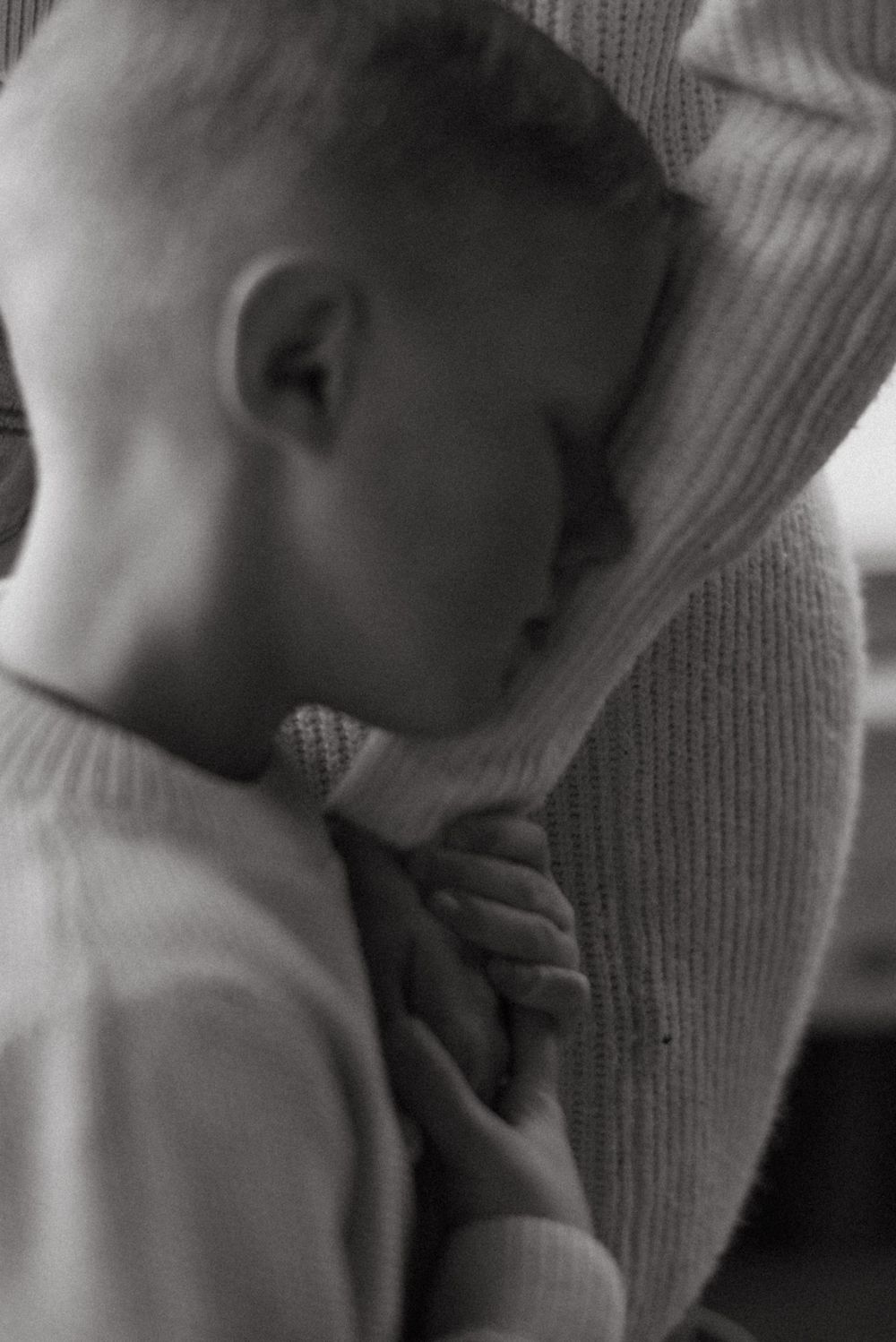 Close-up black and white shots capturing gentle moments between infant and caregiver in soft knitwear.