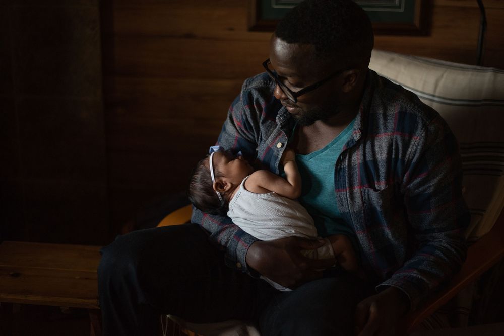 A dimly lit indoor scene showing intimate family bonding moments in low-key lighting.